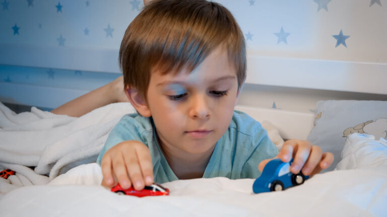little boy playing with cars at bedtime