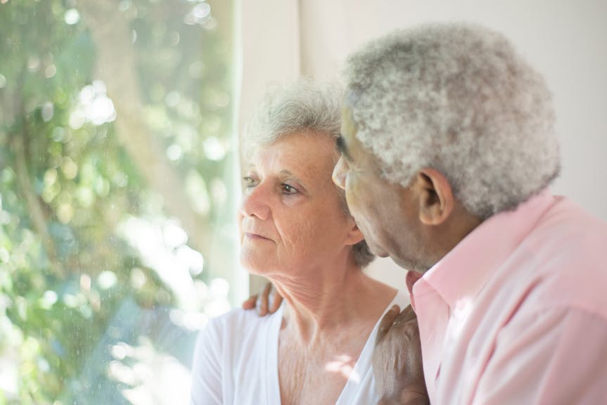 Elderly couple embracing tenderly by a window, reflecting love and support.