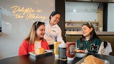 Two women enjoy a meal at a trendy restaurant, served by a friendly waitress.