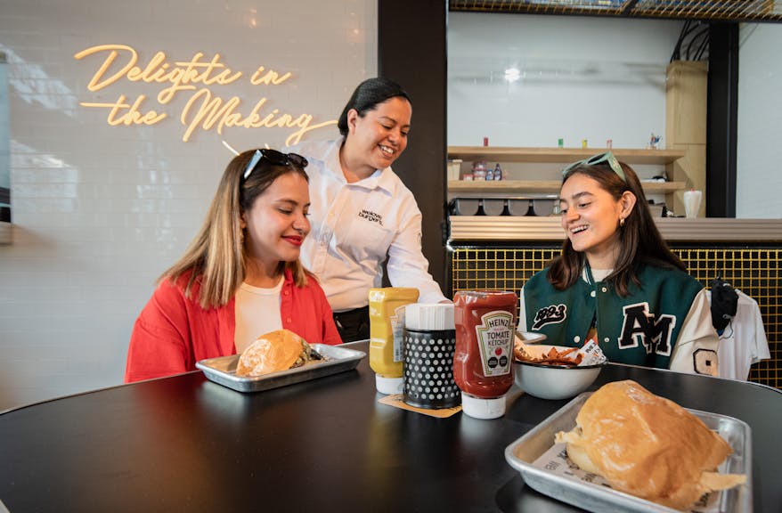 Two women enjoy a meal at a trendy restaurant, served by a friendly waitress.