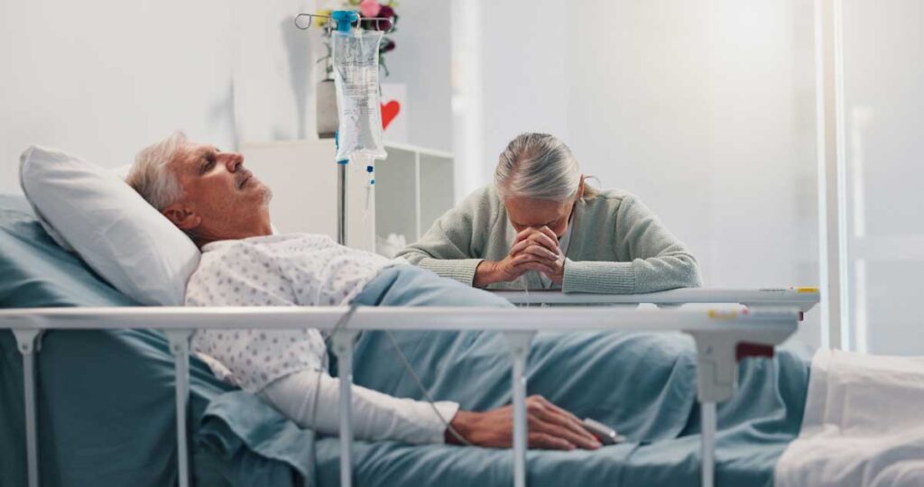 wife praying over husband in hospital bed