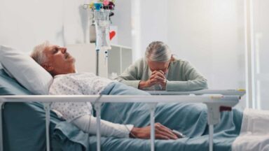 wife praying over husband in hospital bed
