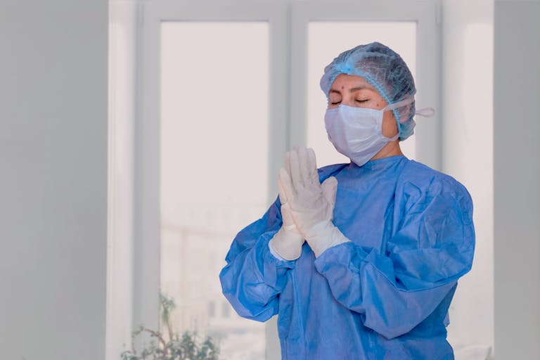 A healthcare worker in protective gear with praying hands, indoors.