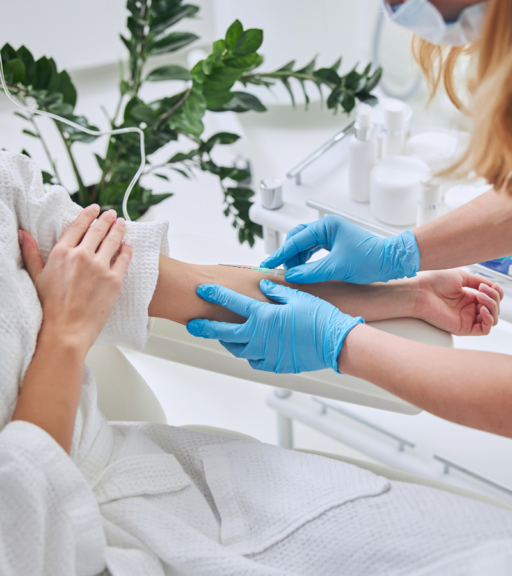 Clinician wearing blue gloves starts an IV line in a patient’s arm for infusion treatment in a clean medical clinic setting.