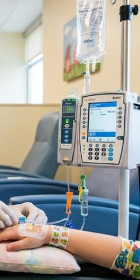 Pediatric patient receiving IV infusion therapy with an infusion pump and fluid bag in a clinic treatment room