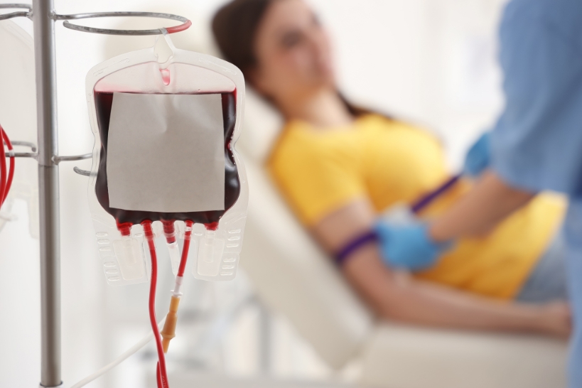 Blood transfusion bag hanging on an IV pole with patient resting in the background during a medical treatment procedure