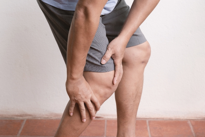 Person holding the lower leg and ankle, illustrating leg muscle weakness that may occur among the signs and symptoms of myasthenia gravis.