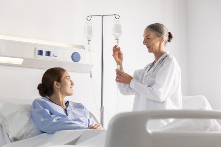 Patient receiving infusion therapy while clinician adjusts IV treatment in a hospital room.